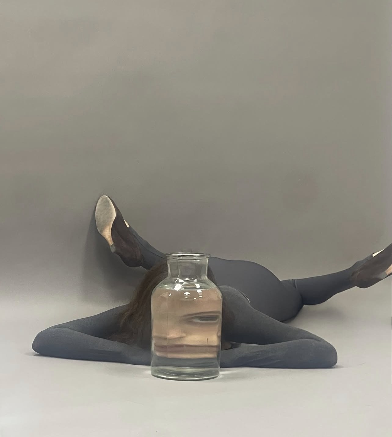 Model sprawled on a grey studio floor behind a water-filled jar